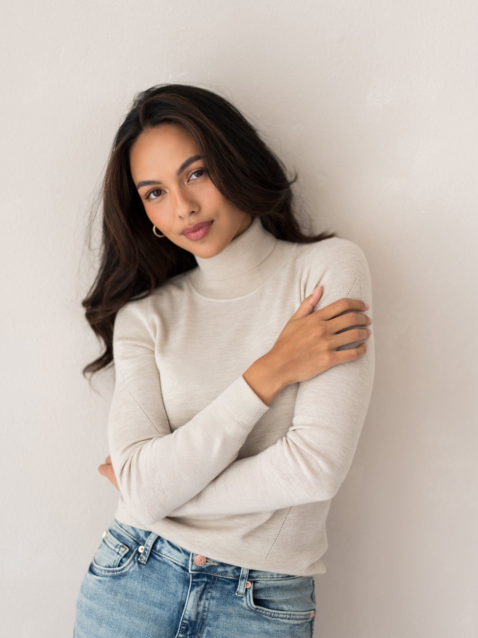 Woman wearing PLEIN PUBLIQUE Merino turtleneck sweater LA FORTE in beige, shown against a light wall.