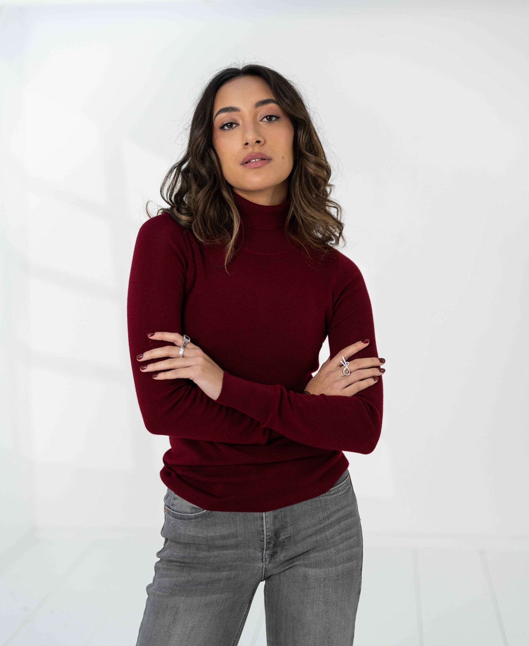 Donkerrode PLEIN PUBLIQUE Merino wool turtleneck LA FORTE, gedragen door een vrouw met golvend haar, armen gekruist.