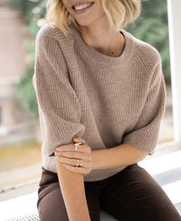 Warm taupe women's sweater by Plein Publique, shown in natural light by a window.