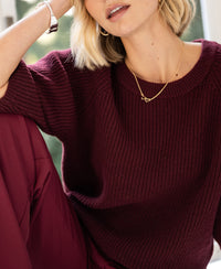 Woman wearing the LA FRAMBOISE wine red sweater by PLEIN PUBLIQUE, seated.