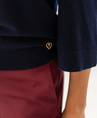 Person wearing the PLEIN PUBLIQUE LE FREJUS dark blue merino wool sweater with a gold heart charm.