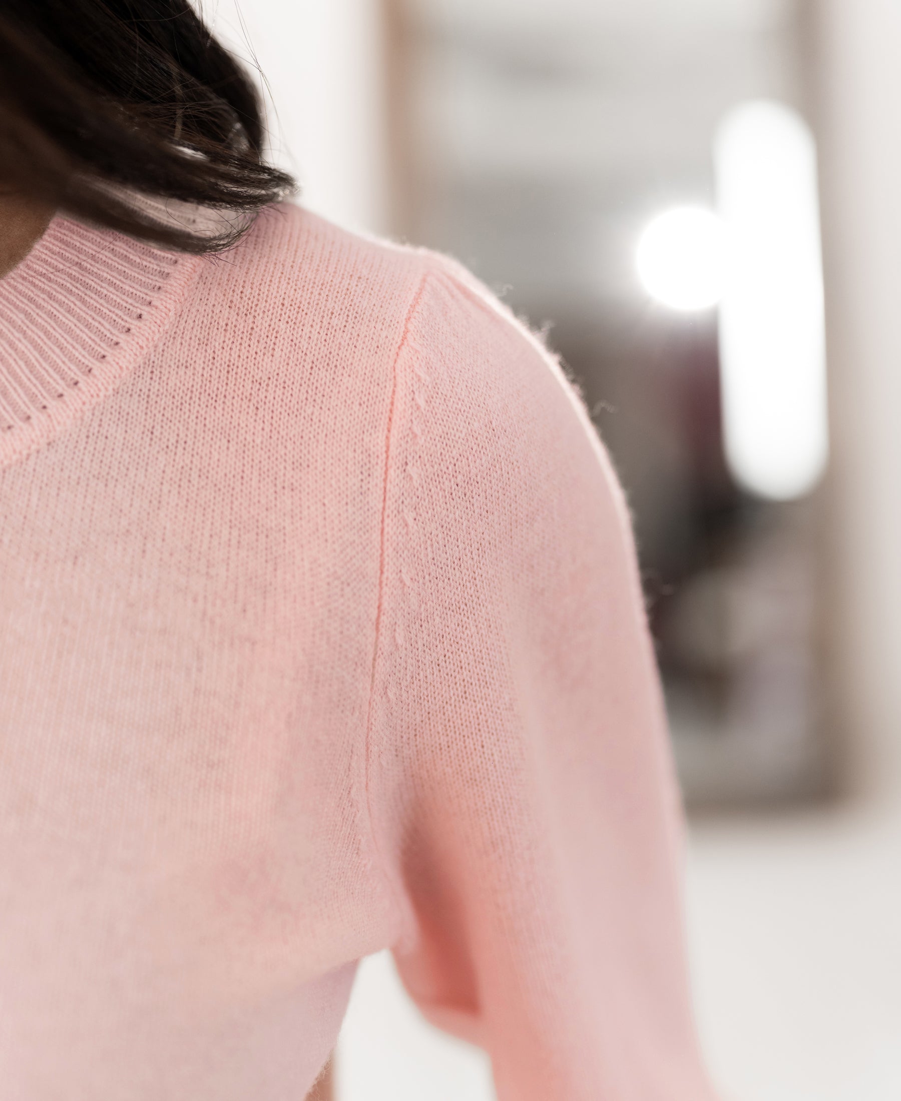 Close-up of the Plein Publique merino wool sweater in light pink, focusing on the shoulder with a blurred background.