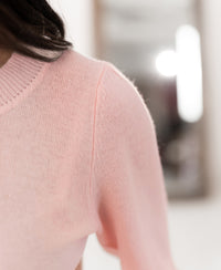 Close-up of the Plein Publique merino wool sweater in light pink, focusing on the shoulder with a blurred background.