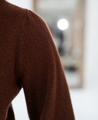 Close-up of a brown merino wool sweater against a blurred, bright background.