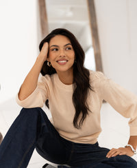 Woman wearing a cream Merino wool sweater, LE FREJUS by PLEIN PUBLIQUE, sitting and smiling.