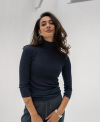 Woman wearing a PLEIN PUBLIQUE LE FABIAN dark blue turtleneck sweater, standing against a white background.