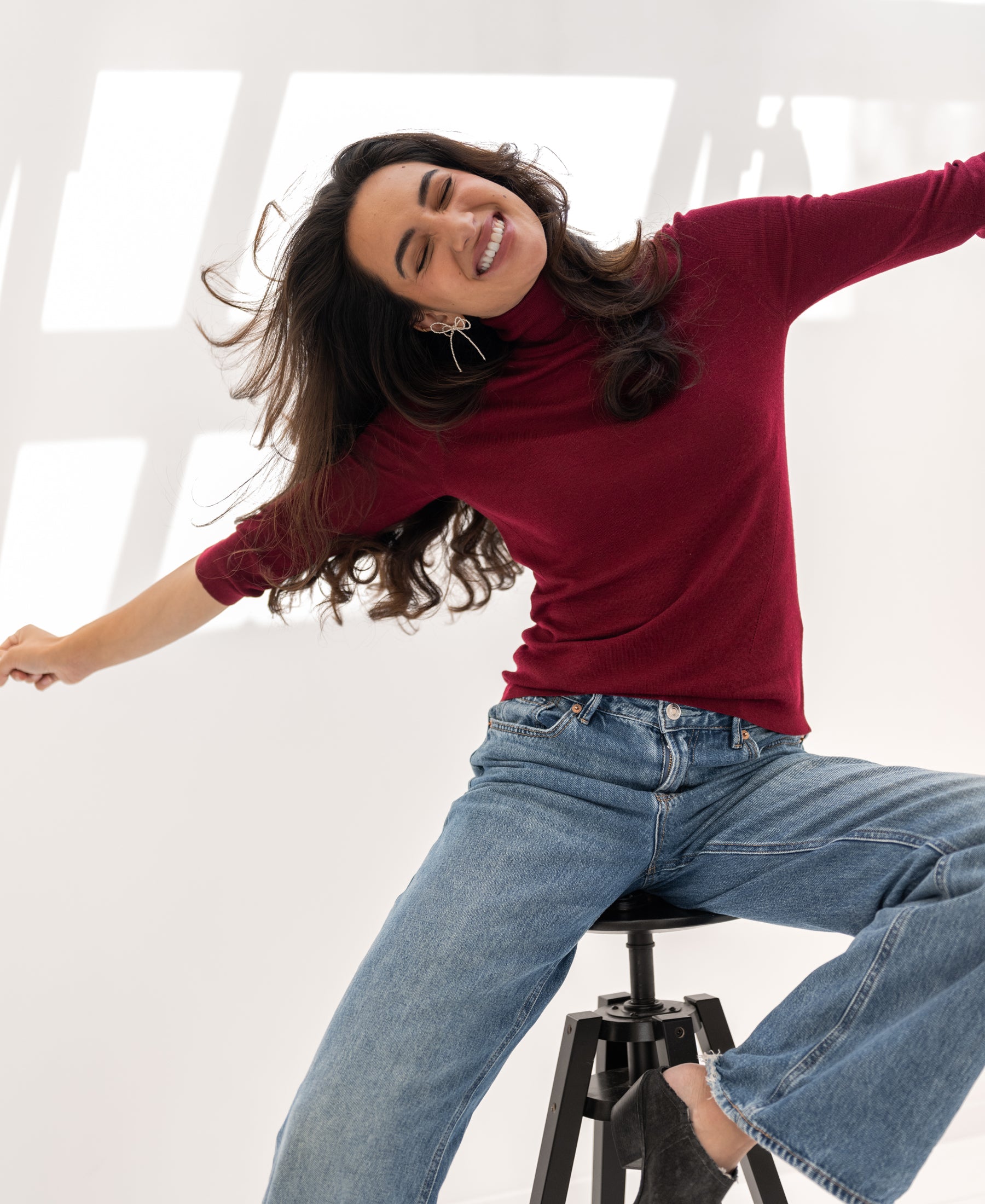 Woman wearing a dark red PLEIN PUBLIQUE LE FABIAN turtleneck sweater, arms outstretched, smiling.