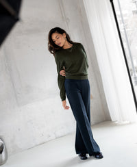 Woman wears the PLEIN PUBLIQUE LA GIGI Merino wool sweater in Bottlegreen, lit by natural window light.