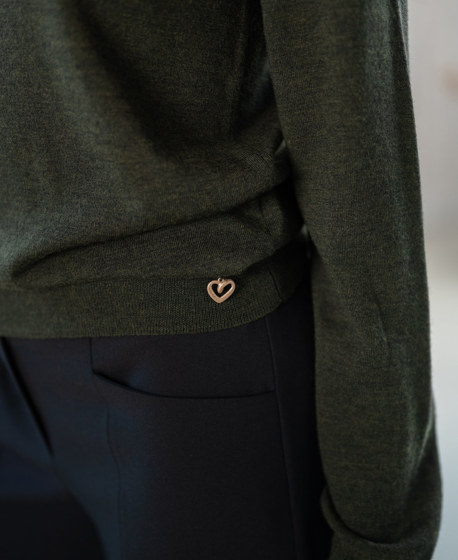 Close-up of a Merino wool LA GIGI sweater in bottlegreen with a heart charm.