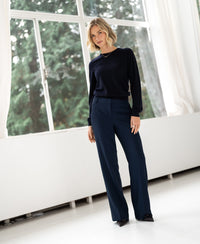 Woman wearing a PLEIN PUBLIQUE dark blue LA GIGI Merino wool sweater, standing in a bright room, facing the camera.