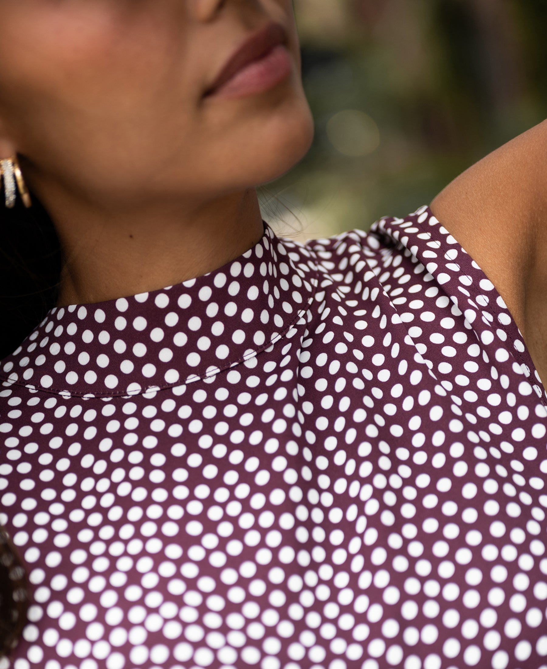 Woman wearing PLEIN PUBLIQUE polka dot blouse LA GIVERNY in wine-ivory, blurred background.