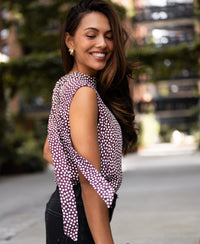 Woman wearing ivory and wine polka dot blouse top, outdoors on a sunny day.