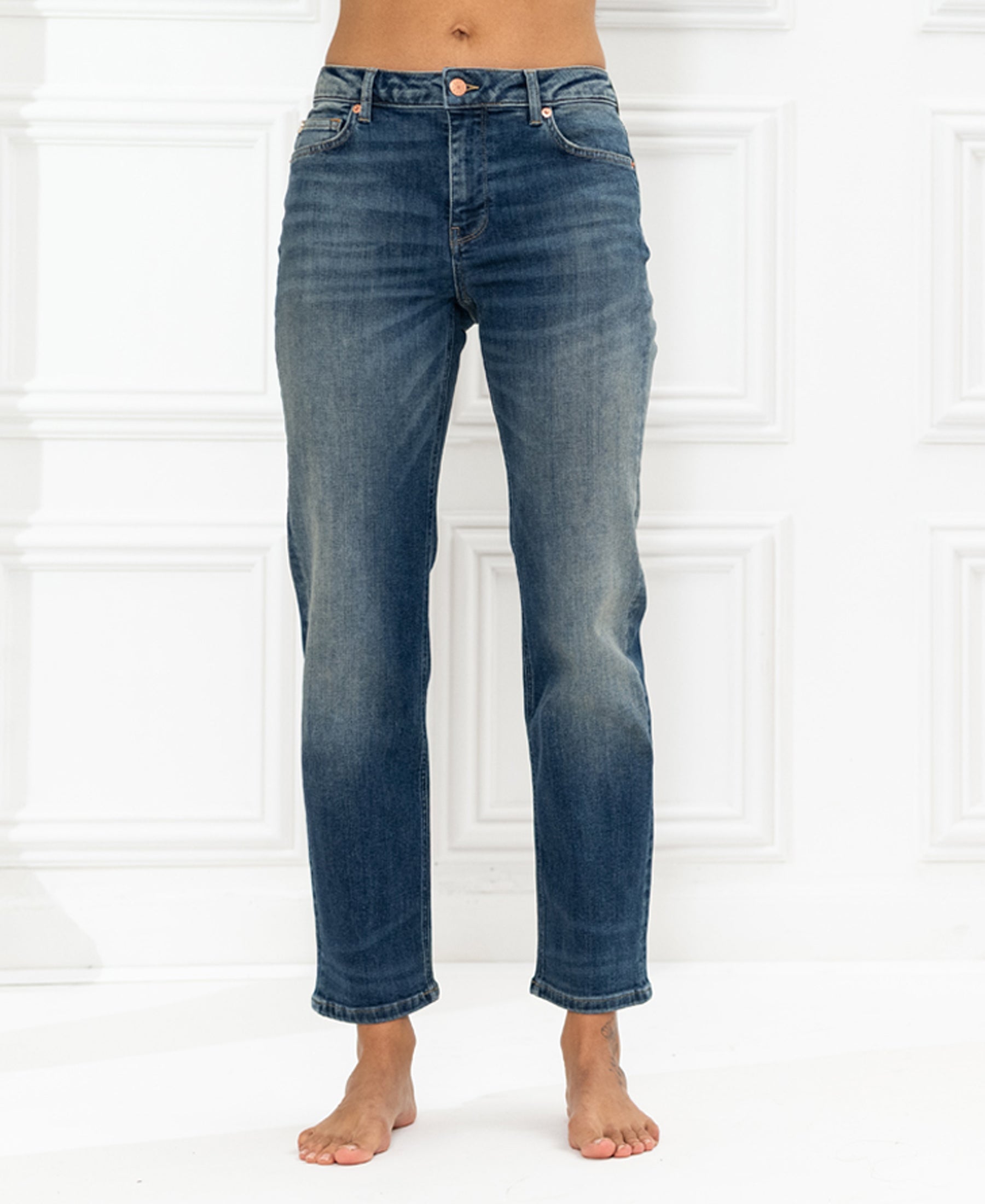 Blue vintage cropped jeans shown from waist to ankles against a white wall.