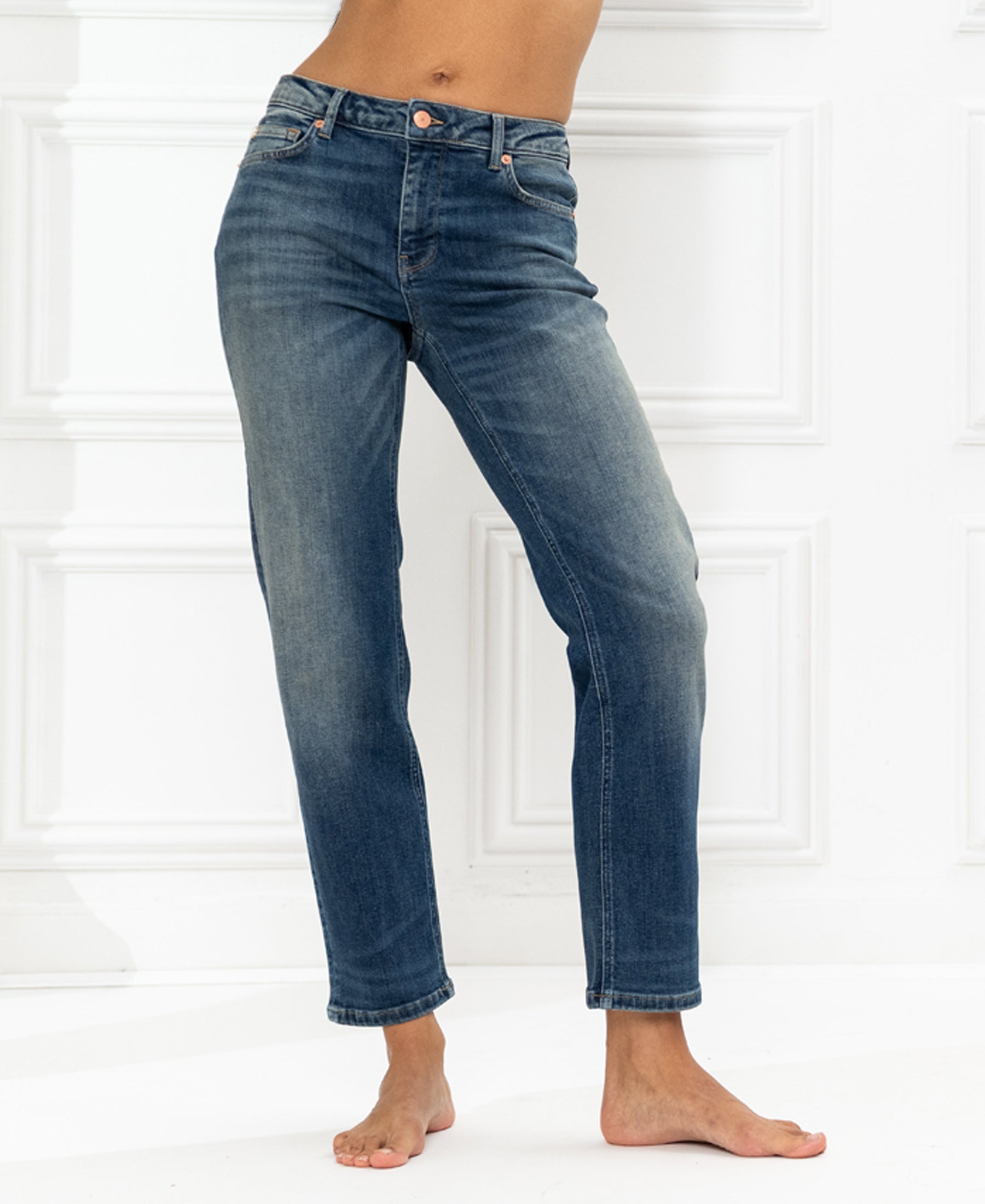 Cropped blue vintage jeans shown from shoulders down against a white wall.