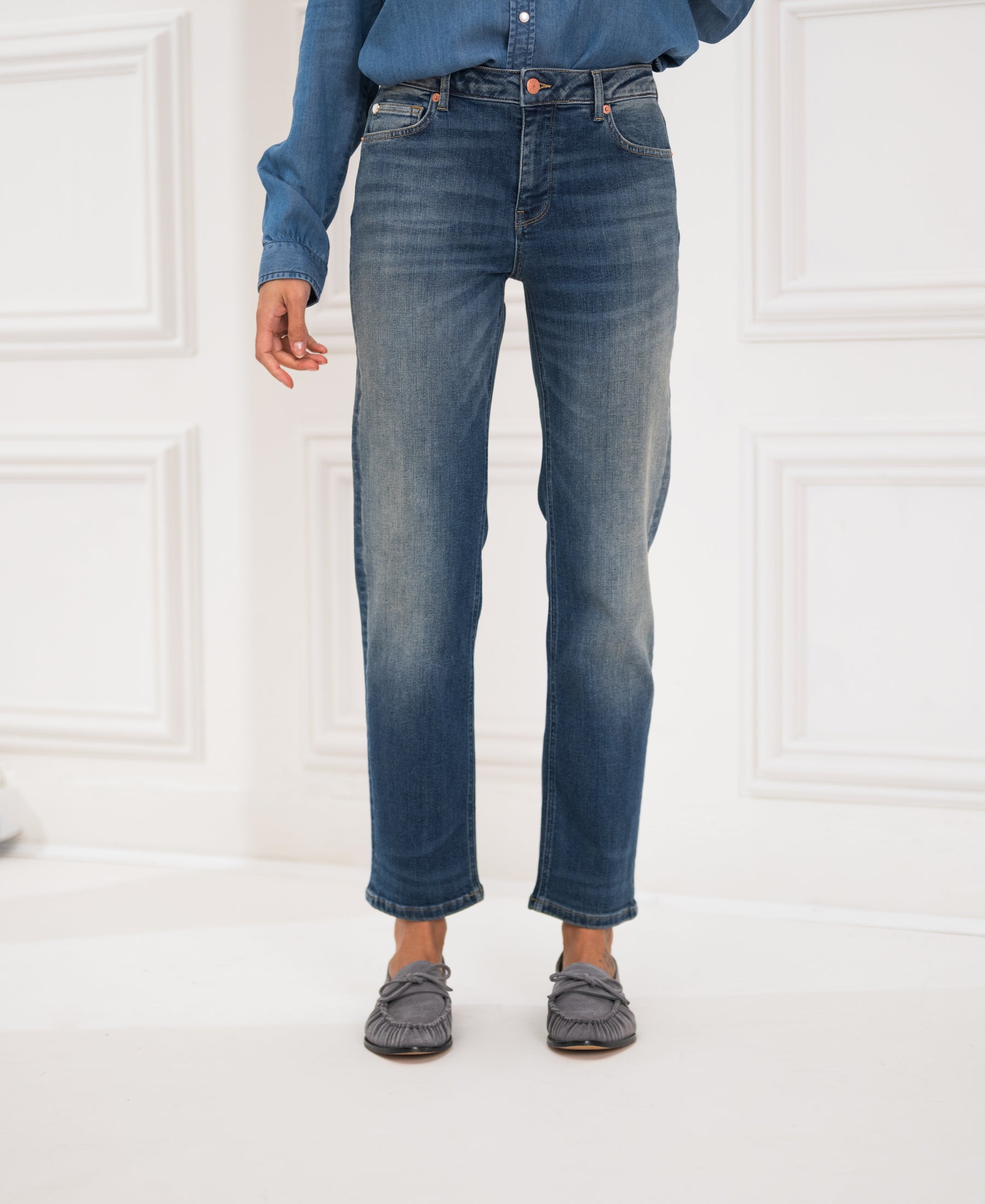 Person wearing cropped blue vintage jeans by a white wall.