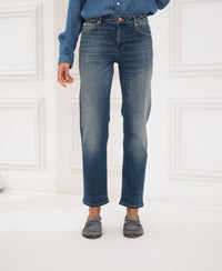 Person wearing cropped blue vintage jeans by a white wall.
