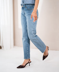Model wears light stone-wash cropped jeans, standing indoors with one leg raised.