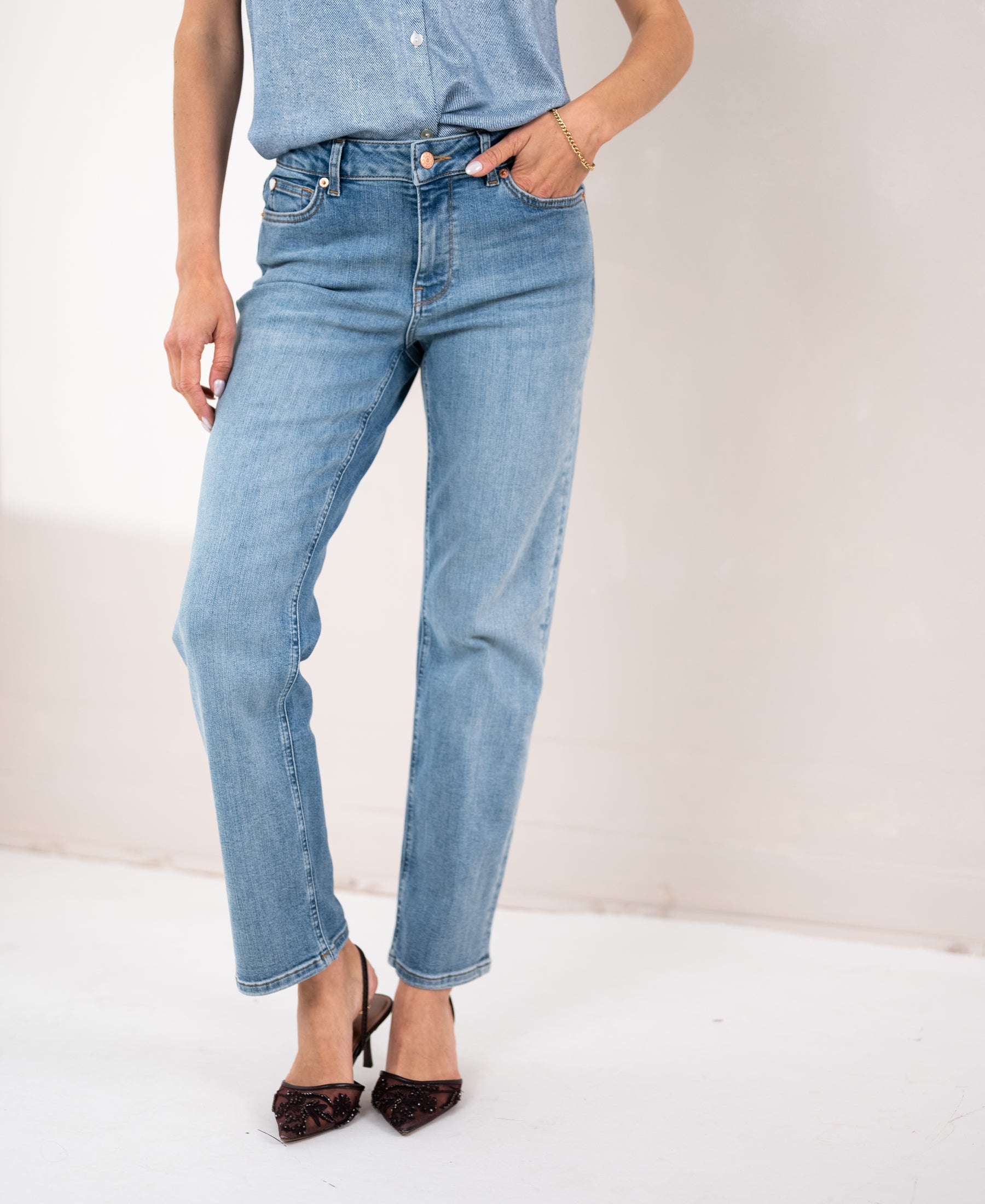 Person wearing light stone wash cropped jeans with a hand in their pocket.