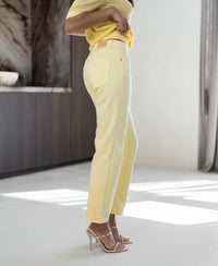 Woman wears PLEIN PUBLIQUE Cropped jeans LE GUY Zacht Geel and matching top, posing sideways in a sunlit room.