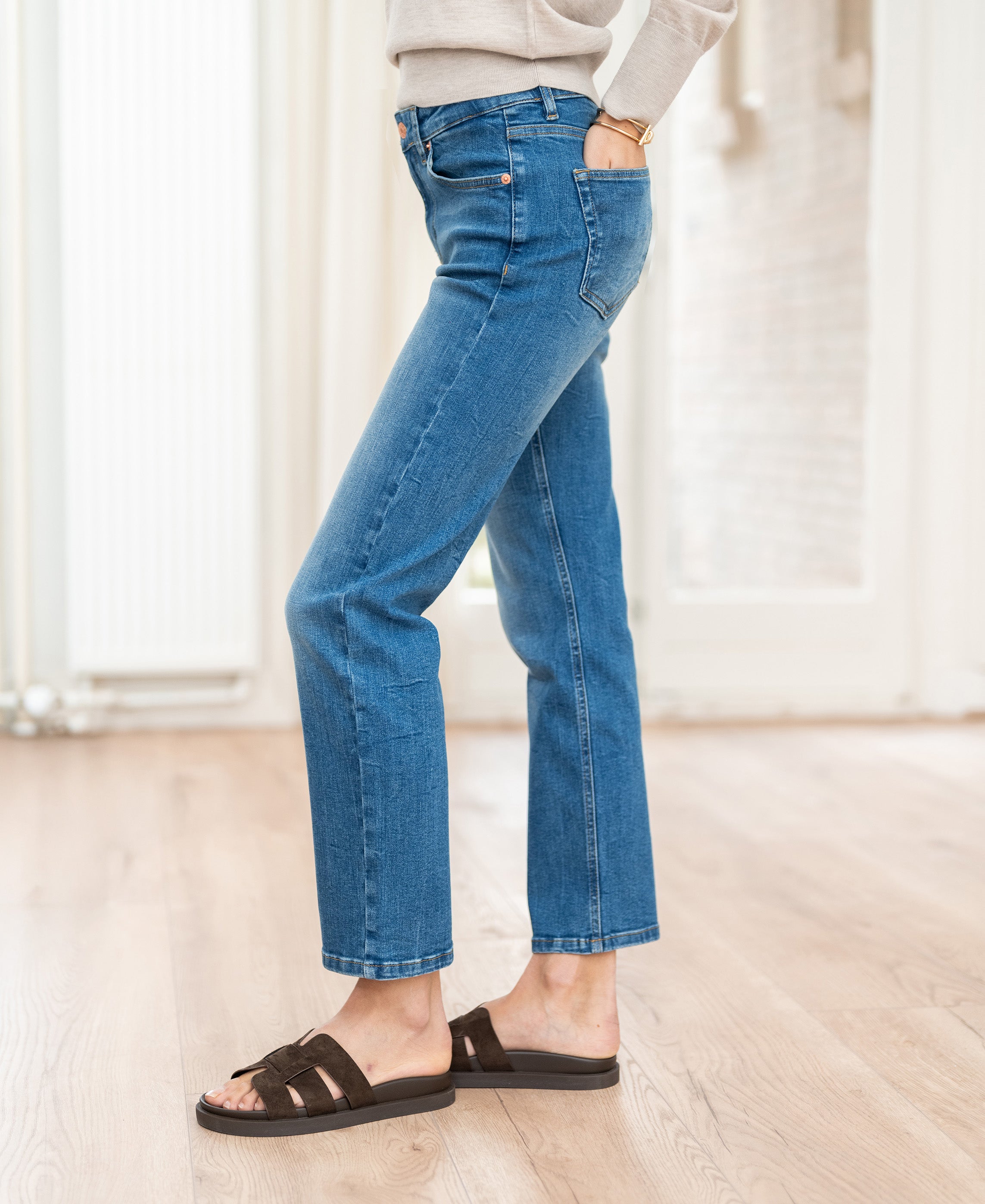 Person wearing cropped stonewash jeans indoors on a wood floor.