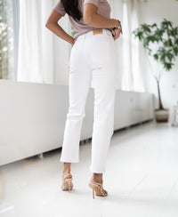 Woman indoors wearing white cropped jeans in a bright modern room.