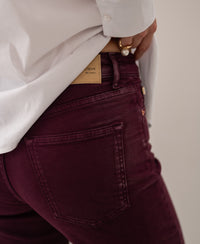 Person wearing wine red cropped jeans, hand on waistband near back pocket.