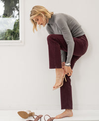 Cropped jeans in a wine color, shown on a model standing by a window and white wall.
