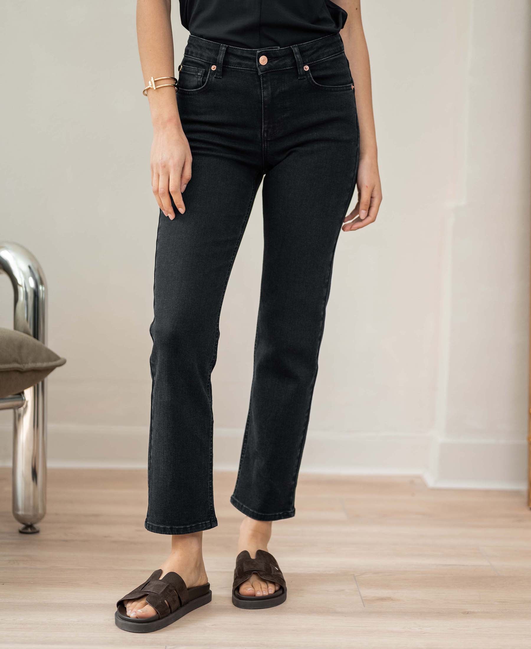 Person wearing black cropped 7/8-length jeans on a light wood floor indoors.
