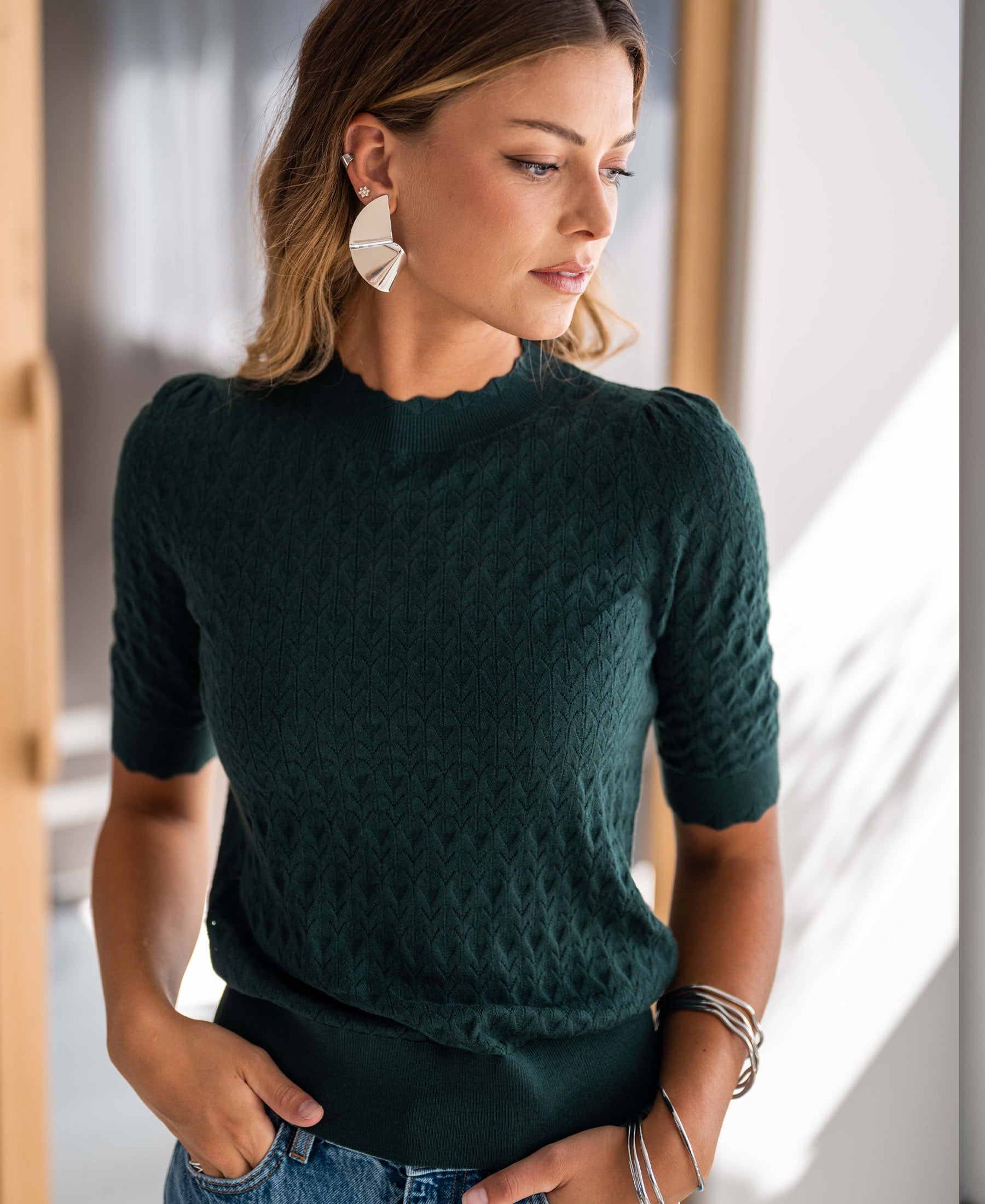 Woman wearing dark green LA BRIOCHE merino wool sweater by PLEIN PUBLIQUE, shown from the side.