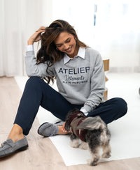 A dog wearing the PLEIN PUBLIQUE LA HARPER light grey sweater is being petted by a woman.