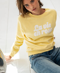 Woman wearing a yellow PLEIN PUBLIQUE LA HARPER sweater sits on a white floor, looking up.
