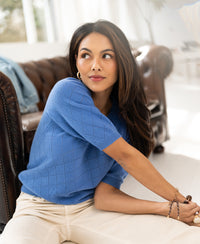 Lavender argyle merino wool sweater with a crew neck, shown being worn seated.