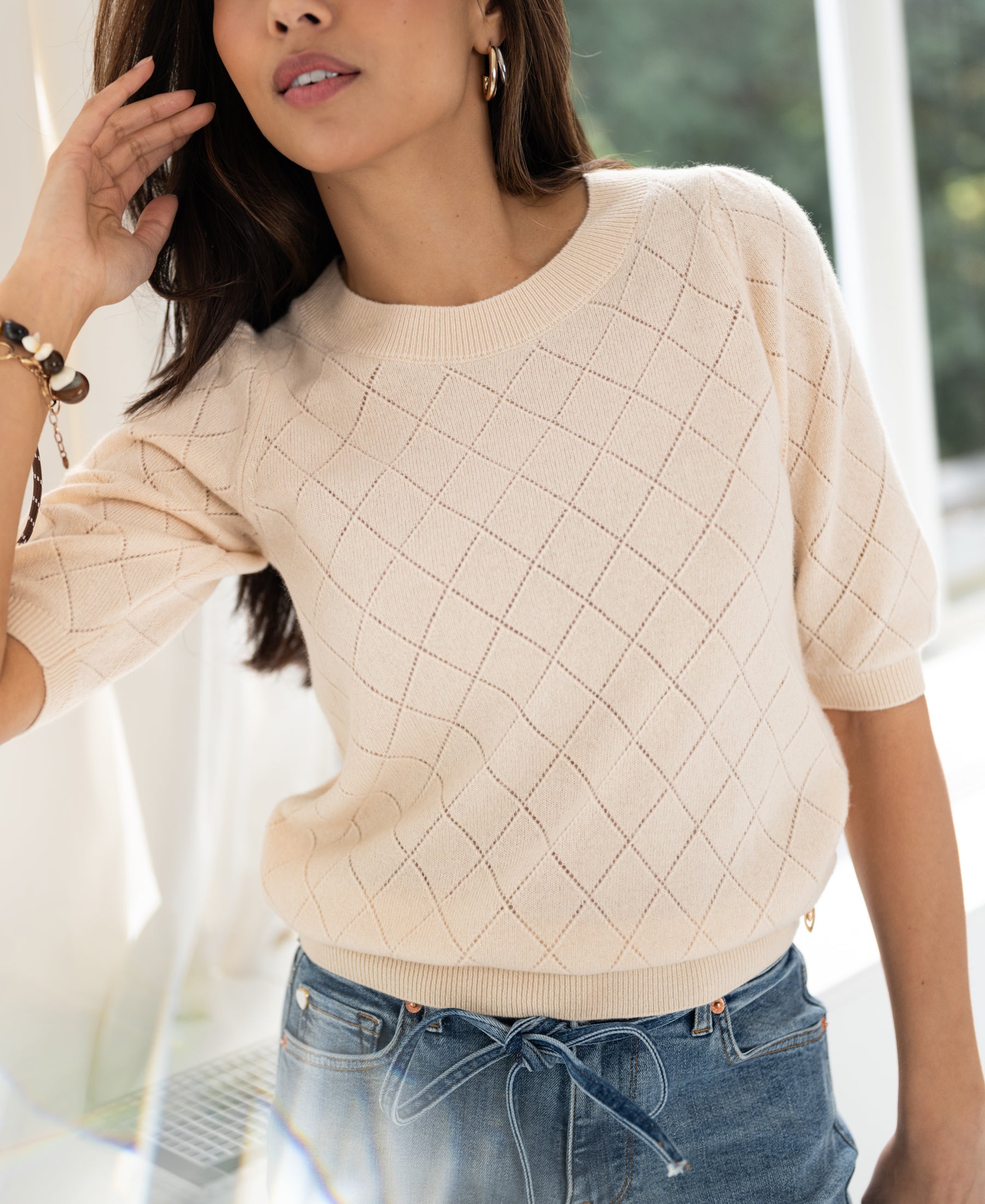 Woman wears the Argyle merino wool sweater in butter yellow from PLEIN PUBLIQUE in a bright room.