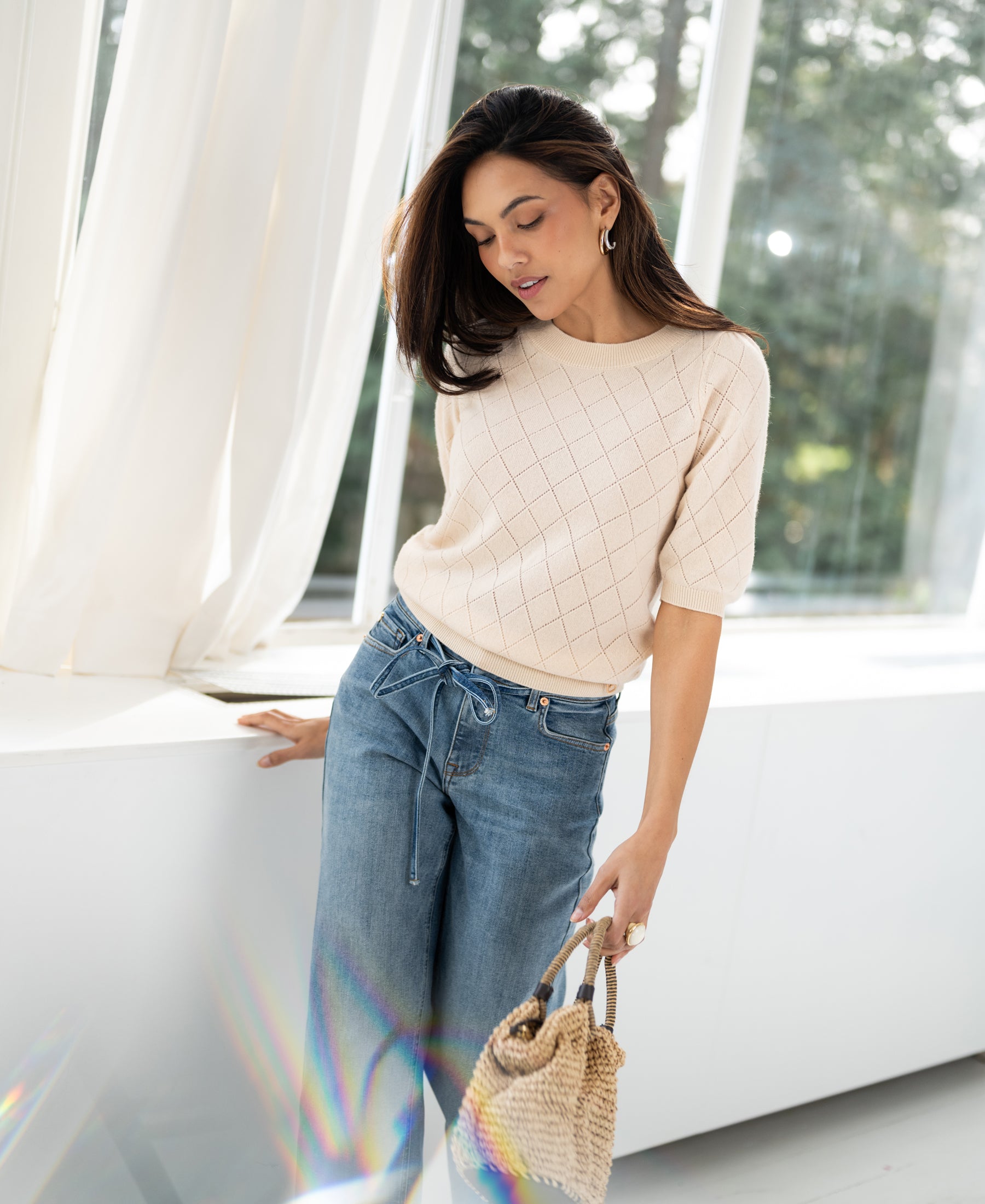 Woman wearing the Argyle merino wool sweater "The Harvard" in butter yellow by Plein Publique, standing by a sunny window.