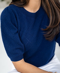Navy argyle merino wool sweater by Plein Publique, shown on a seated model.