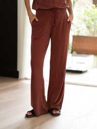 Person wears henna-colored LE HUGO lounge pants by PLEIN PUBLIQUE, standing indoors with hands in pockets.