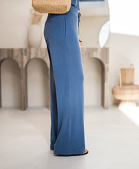 Lounge pants LE HUGO in jeans blue by PLEIN PUBLIQUE, worn by model; blurred furniture in the background.