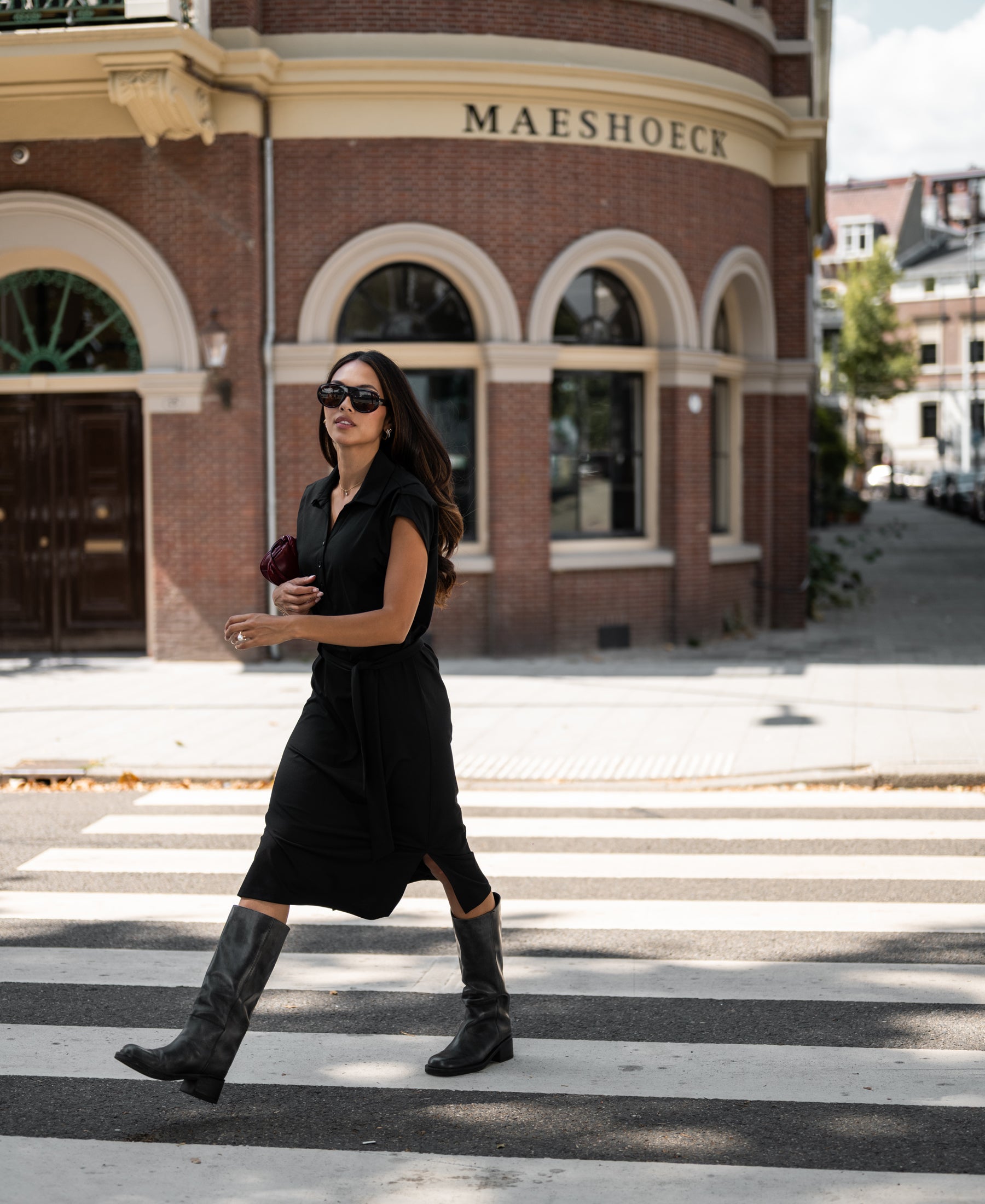 Black INES Travel polo dress by PLEIN PUBLIQUE shown on a woman crossing the street.