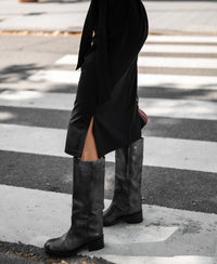Person wearing the PLEIN PUBLIQUE black INES travel polo dress stands confidently at a city crosswalk.