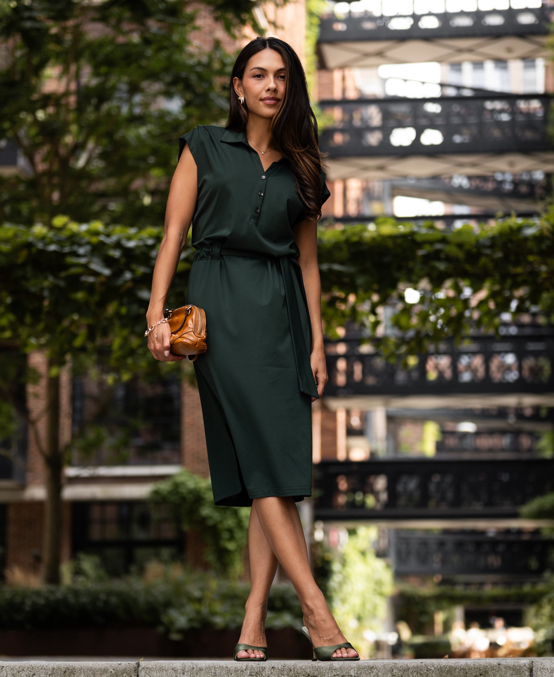 Woman wearing a dark green travel polo dress stands outside with greenery in the background.