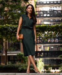 Woman wearing a dark green travel polo dress stands outside with greenery in the background.