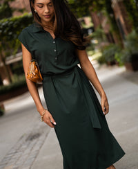 Woman wearing a dark green PLEIN PUBLIQUE Travel polo dress, lush greenery in the background.