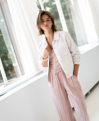 Woman standing indoors by large windows, wearing white denim LA JACKY jacket from PLEIN PUBLIQUE, hand in pocket.