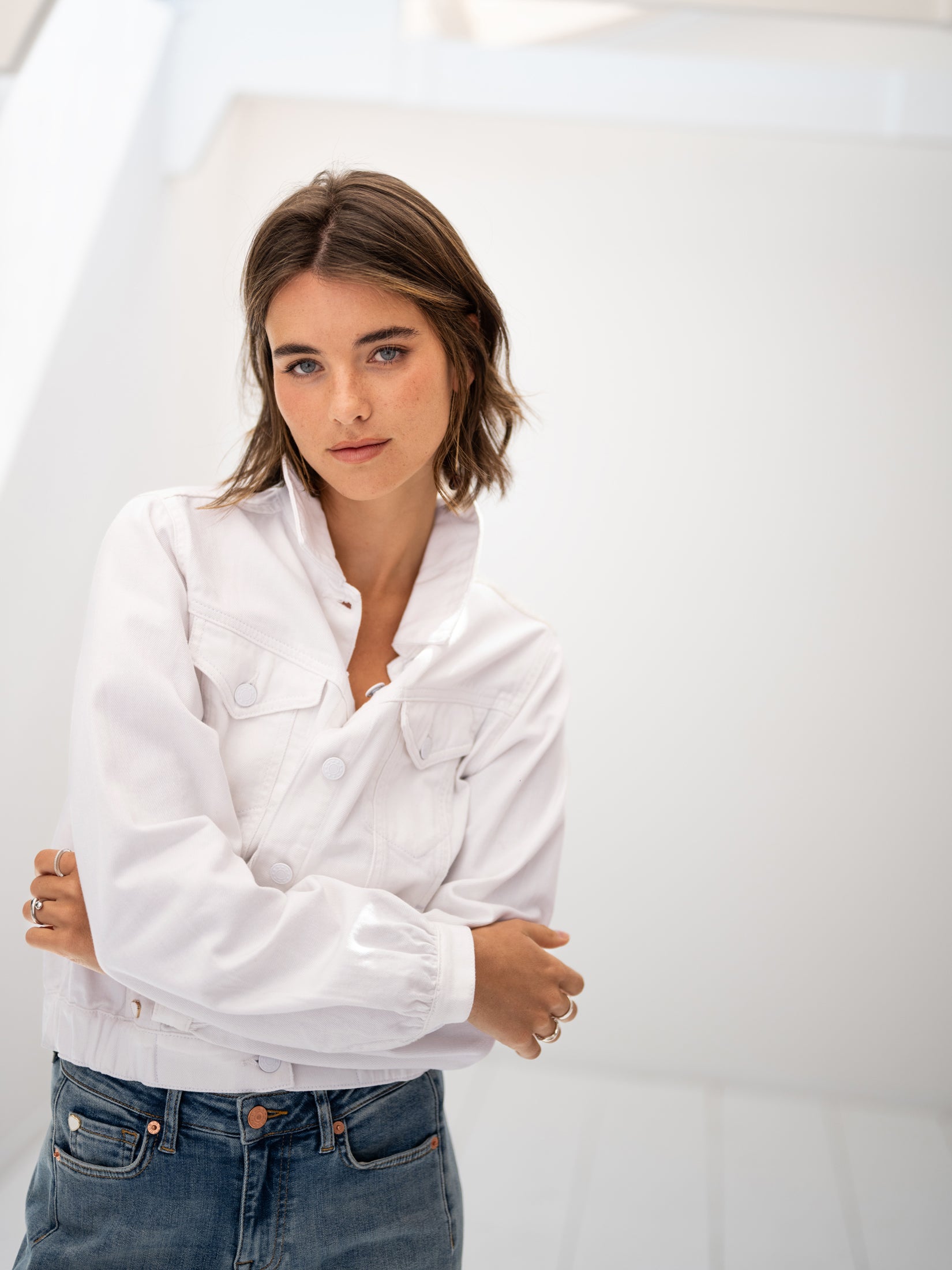 Front view of the Plein Publique LA JACKY white denim jacket, shown on a woman with folded arms.