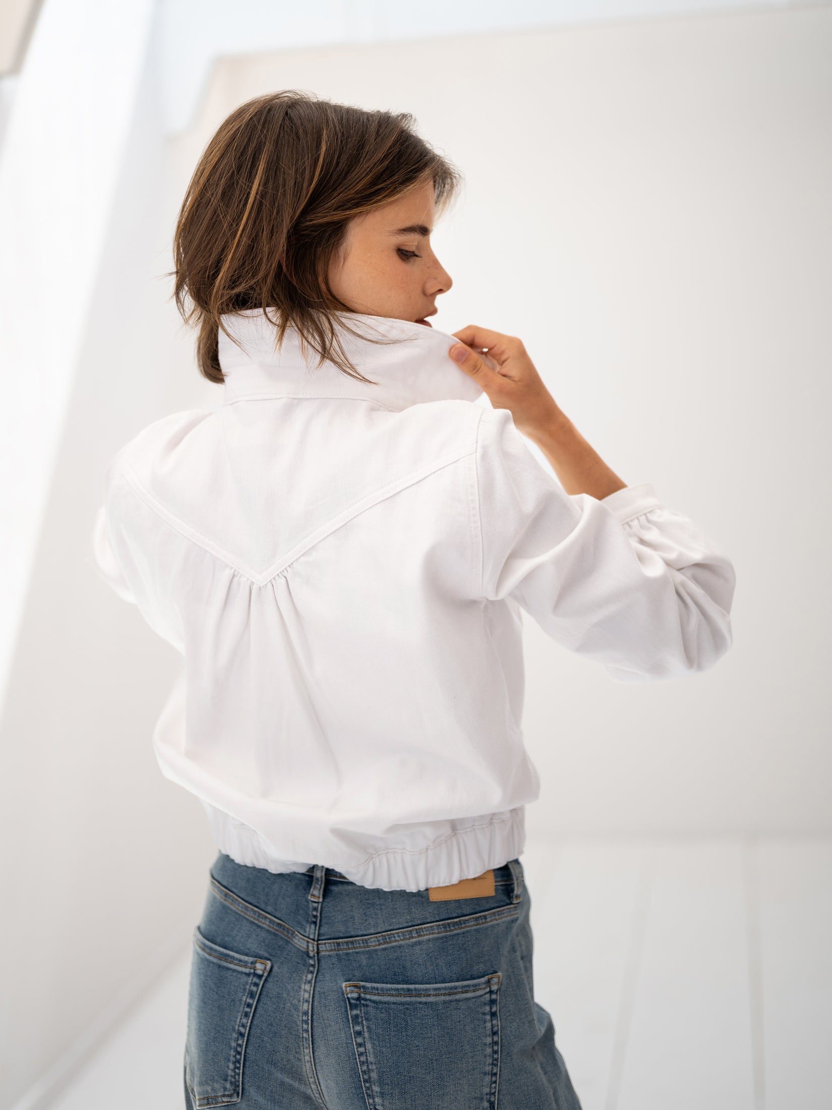 White denim jacket shown from the side, collar held by model.
