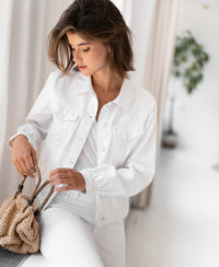 White denim jacket displayed by white curtains and a green plant.