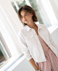 White denim jacket, front view, shown on a woman standing by a sunny window.