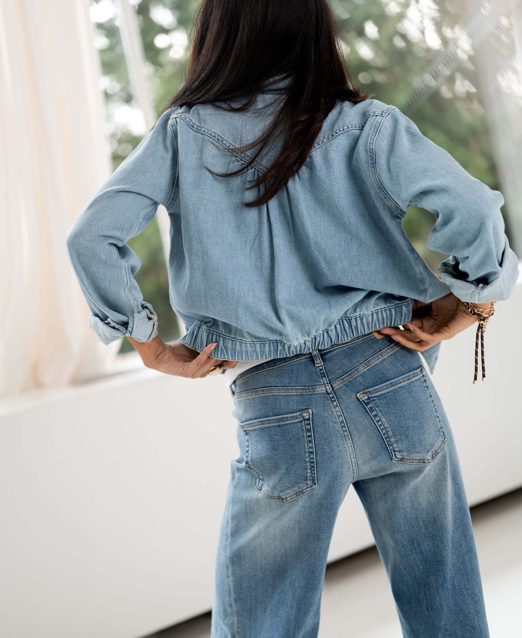 Wide leg jeans in light stone color, shown from the back with hands on hips.