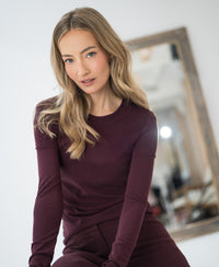 Woman wearing PLEIN PUBLIQUE Luxe long sleeve T-shirt LA JANE in wine color indoors by a blurred mirror.