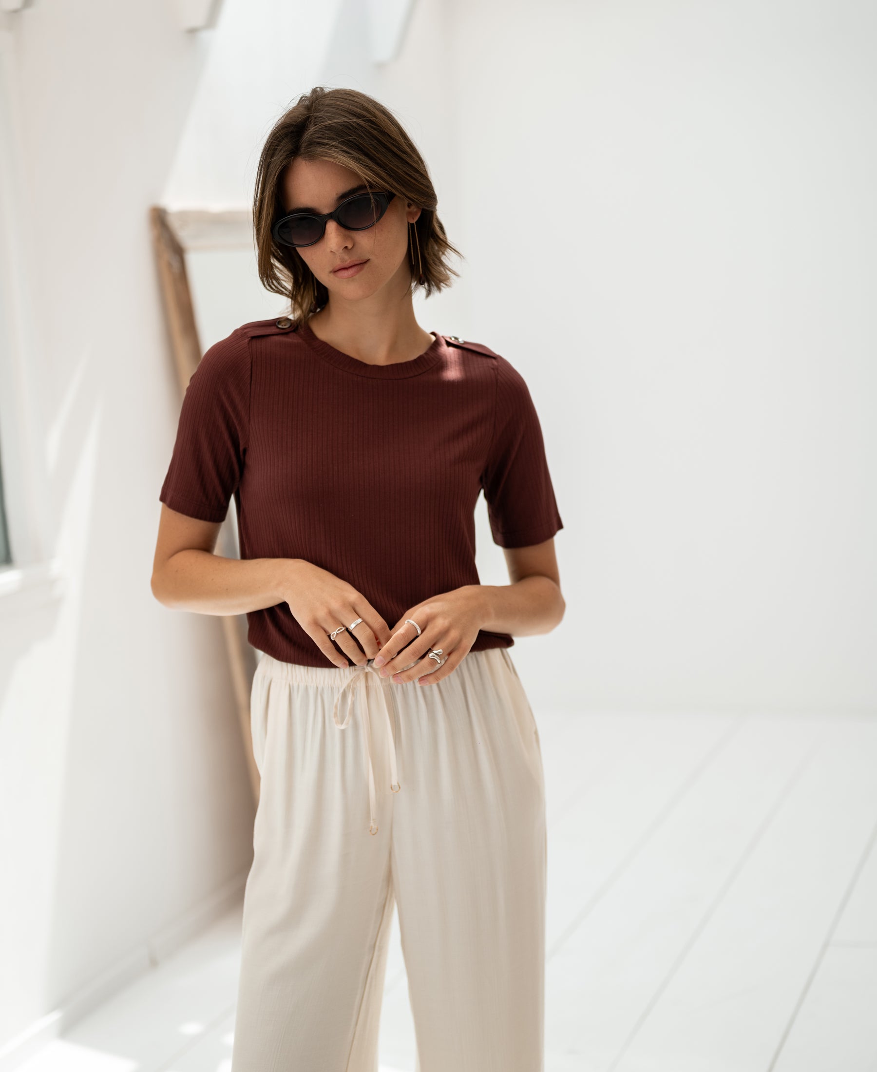 Woman wearing a bamboo T-shirt in reddish brown by Plein Publique, shown in a bright minimalist room.